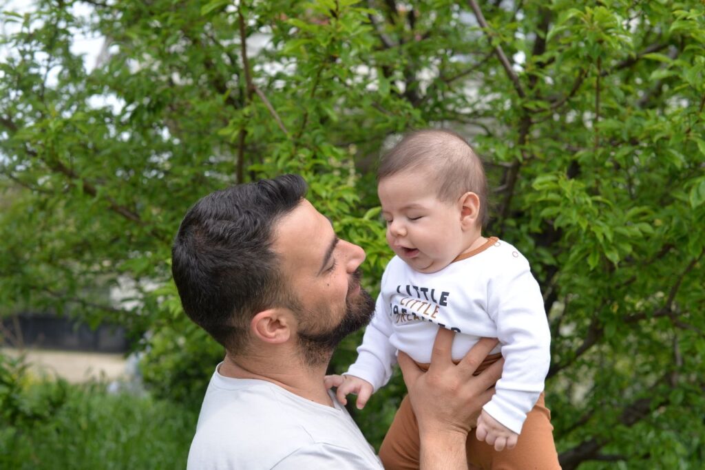 A loving father holds his baby son outdoors amidst lush greenery, showcasing fatherhood and care.