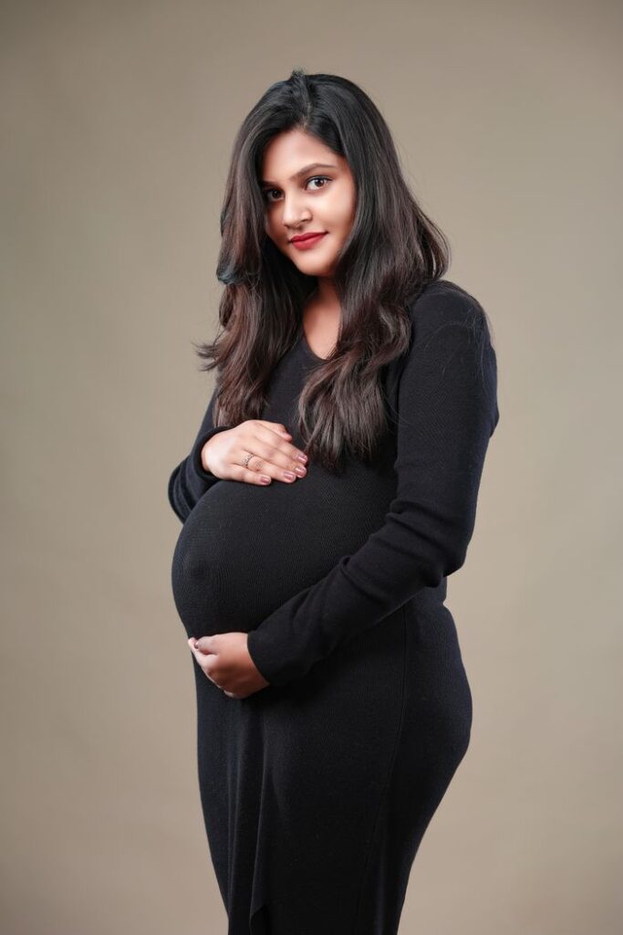 Portrait of a smiling pregnant woman in a black dress, captured in a studio setting.