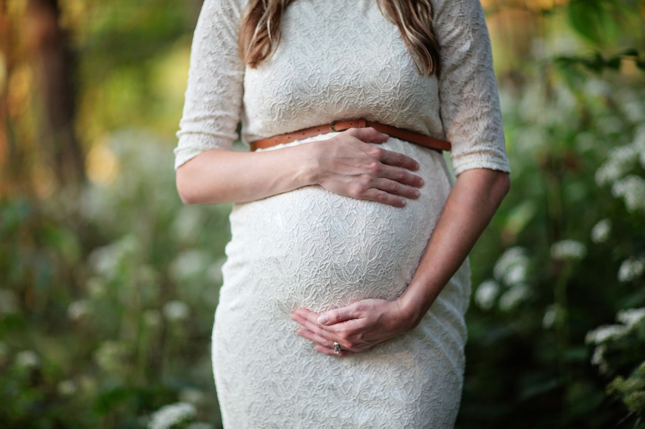 A pregnant woman in a lace dress gently cradling her belly in an outdoor setting for Prenatal Paternity Process image by EVIDEXA DNA Test Solution Pvt Ltd
