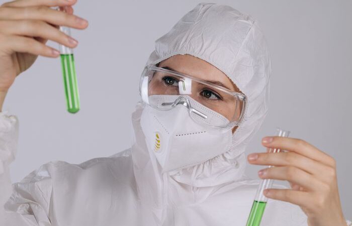 Scientist examines green liquid in test tubes with protective gear on.