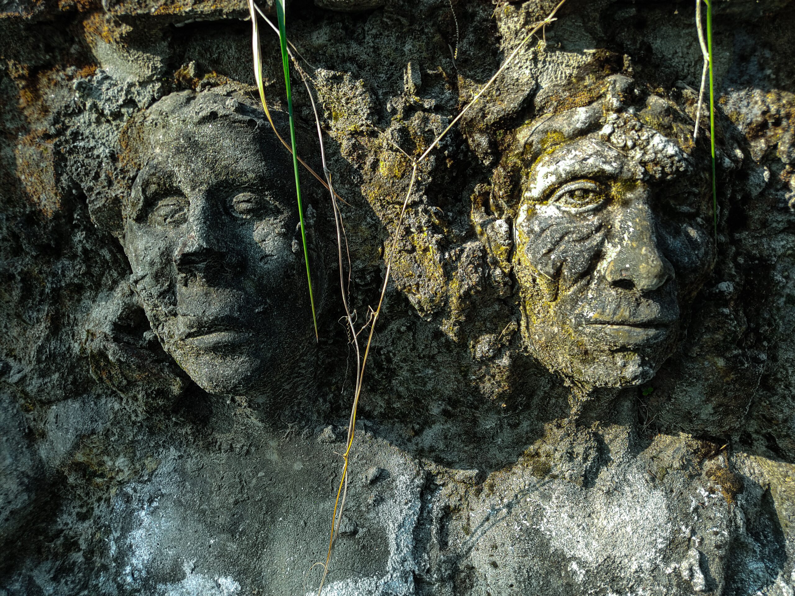 Close-up of ancient stone face sculptures embedded in a textured wall. Ancestry DNA Test By EVIDEXA DNA Test Solution Pvt Ltd